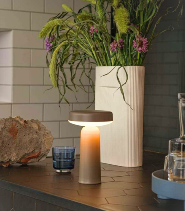 Draagbare Muuto tafellamp op een donker keukenblad met bloemendecoratie.