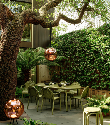Tom Dixon buitenlampen in stijlvolle tuin met eethoek onder oude boom.