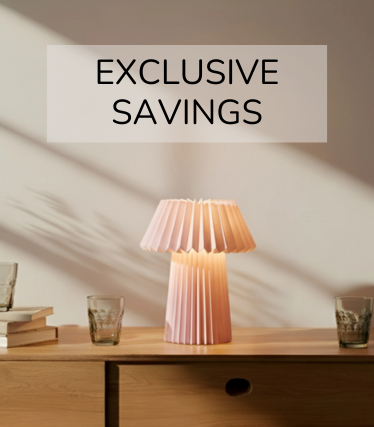 Lichtroze tafellamp op een houten dressoir, omringd door glazen en boeken in het warme zonlicht.