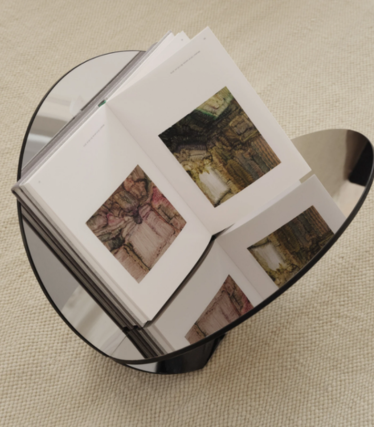 Ronde bijzettafel van donker glas met een opengeslagen kunstboek, op een beige vloerkleed.