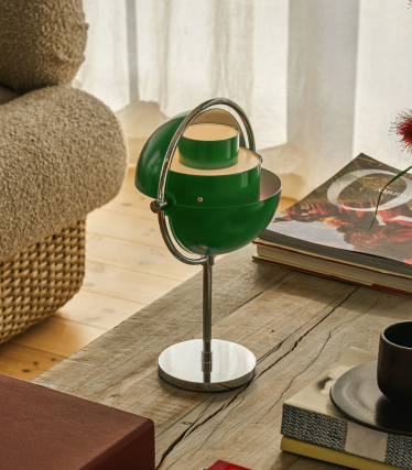 Groene Multi-Lite tafellamp met chromen voet op een houten tafel naast boeken.