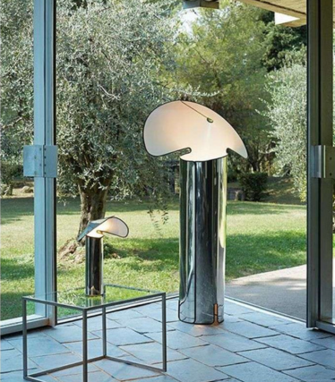 Twee glanzende vloerlampen met gebogen, bladvormige kappen voor een raam met uitzicht op de tuin.